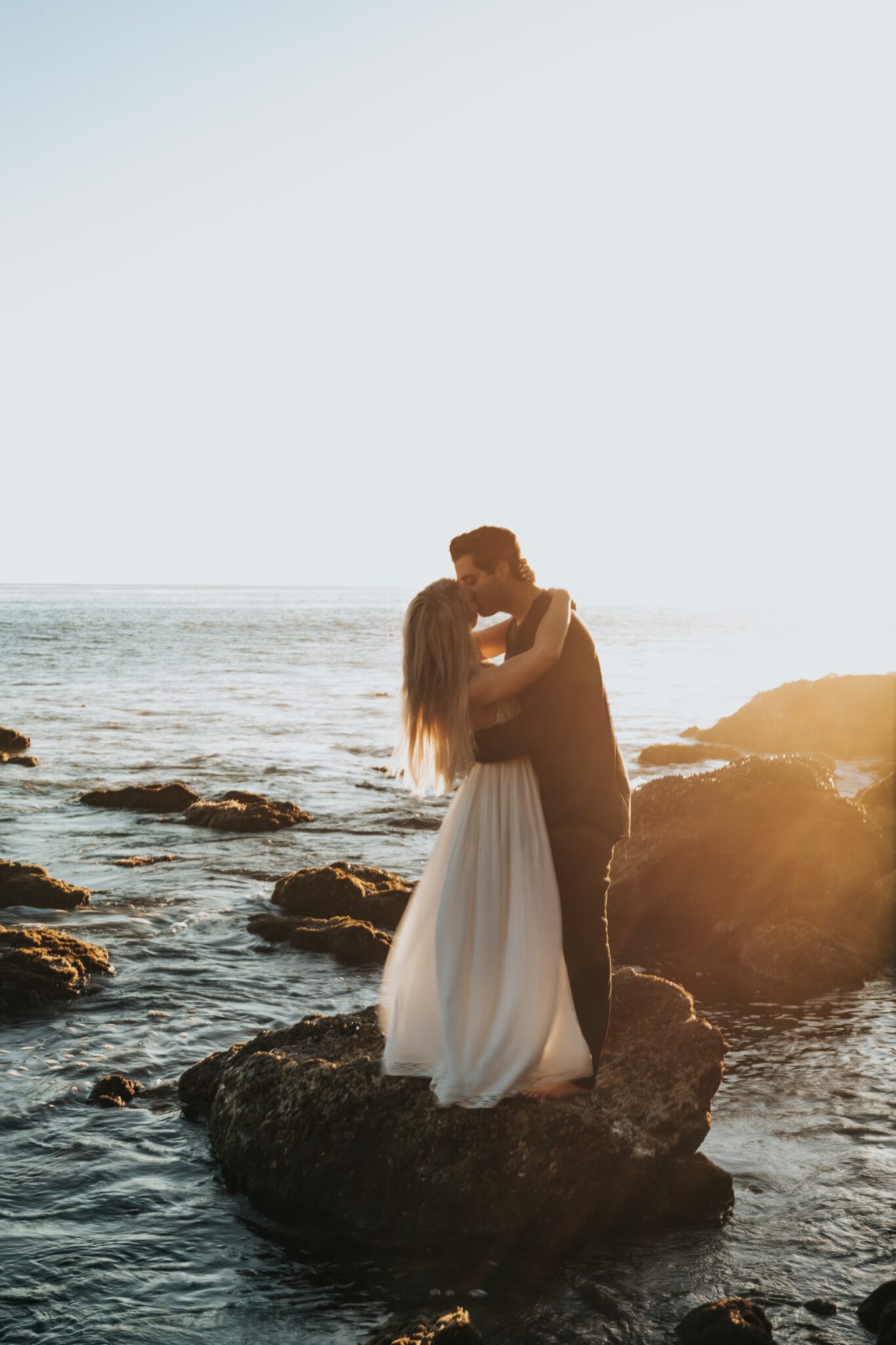 Bröllopsfoto på kyssande bröllopspar på stenblock mitt i vattnet